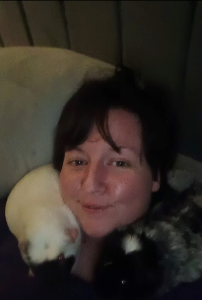 Potrait of Rosie with two guinea pigs snuggling against her neck. She has dark hair and smiles. 